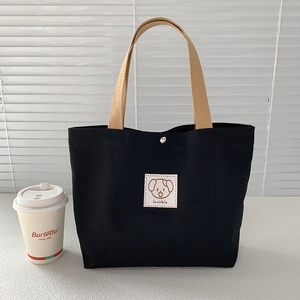 Close-up of black canvas tote bag with a lovable puppy patch and khaki strap on a desk