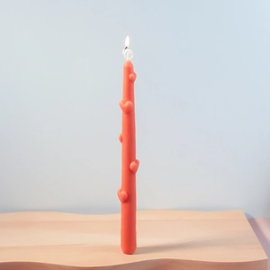 Vela de columna rosa con corazones encendida sobre base de madera con llama suave