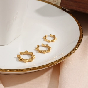 Detailed view of three gold-plated rivet ear cuffs on a luxury porcelain tray