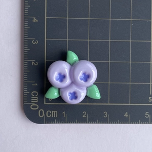 Size measurement of a purple resin blueberry charm with green leaves on a ruler mat