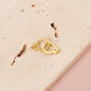 Macro detail of interlocking gold handcuff pendant on a textured stone surface