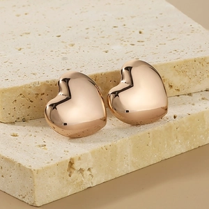 Macro detail of rose gold heart stud earrings on beige stone showing polished metal finish
