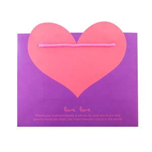 Detail of purple paper gift bag featuring a large pink heart and love quote on white backdrop