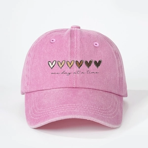 Détail de la casquette en coton délavé rose avec motifs de cœurs et texte one day at a time
