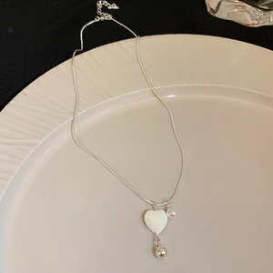 Detail of silver snake chain with heart pendant and pearl on white ceramic plate