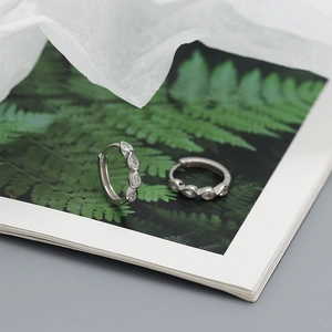 Detail shot of silver S925 huggie earrings with marquise-cut zircons on a leaf background