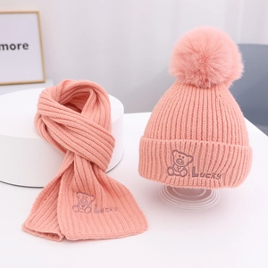 Detailansicht der rosa Strickmütze und des Schals mit Bärenstickerei und Bommel