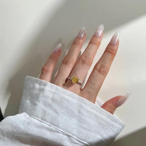 Close-up of heart-cut yellow gemstone ring with side diamond accents on finger