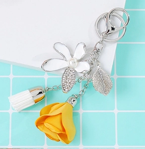 Detailed close-up of a floral keychain with white enamel flower, yellow rose, and tassel