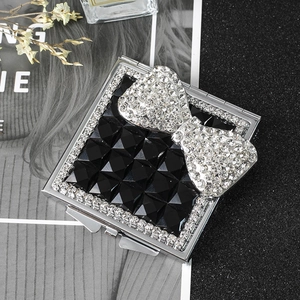 Detail of square silver makeup mirror featuring black gems and a sparkling bow ornament