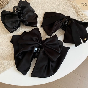 Detailed view of three premium black satin bow hair claws with elegant ribbon textures