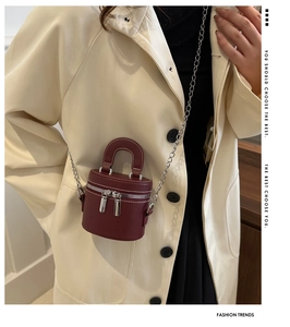 Détail du sac cylindre bordeaux avec chaîne en argent sur un manteau en laine beige