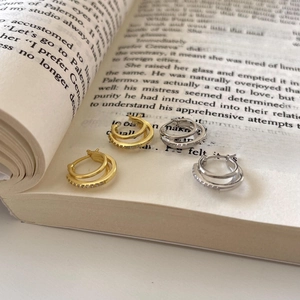 Detail of gold and silver double-hoop earrings with zircon inlay on vintage book pages