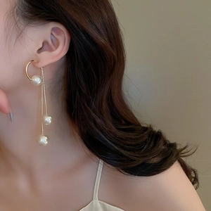 Close-up of elegant gold tassel earrings with white pearls worn by a female model