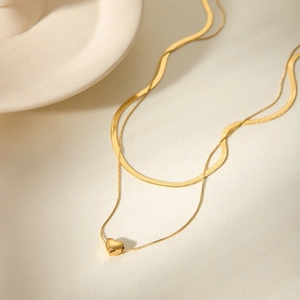 Detailed view of layered 18k gold snake chain and delicate heart pendant necklace