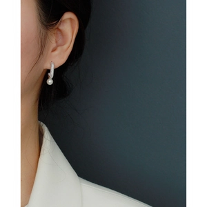 Close-up of silver C-shaped pearl earring with small diamonds on a model's ear
