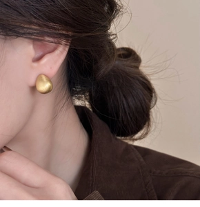 Macro detail of matte 18k gold plated teardrop stud earrings on a model's ear