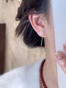 Close-up of silver snowflake earring with zircon stones worn by a model in warm light