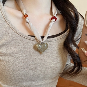 Detail of beige fabric necklace with orange beads and marble textured heart pendant
