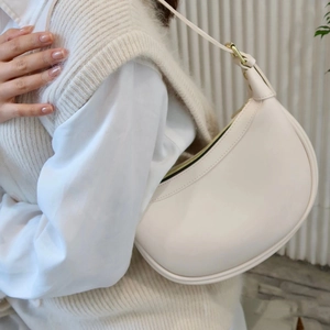 Close-up of a cream ivory crescent bag featuring a sleek matte finish and golden zipper