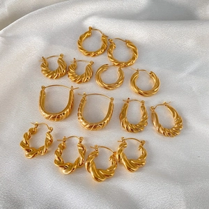 Collection of gold plated stainless steel twisted hoop earrings on white silk fabric