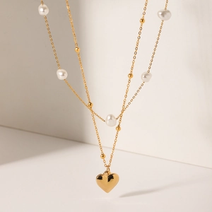 Detail of double-layer gold necklace featuring a polished heart pendant and white pearls