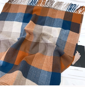 Detail of soft checkered scarf with fringe trim in navy blue, orange, and brown tones