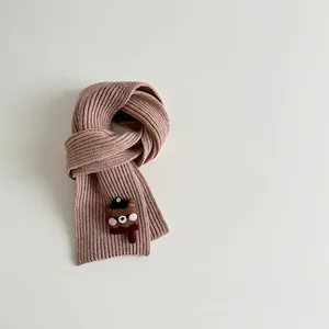 Detailed texture of milk tea knit scarf featuring a cute cartoon bear badge ornament