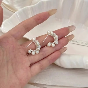Close-up of silver C-shaped earrings with white pearls and sparkling cubic zirconia stones
