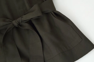 Gros plan d'un manteau en sergé vert olive avec ceinture nouée et détails de poche cousus