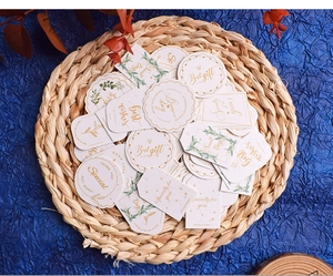 Detail of paper gift tags with gold foil text and botanical prints on a woven mat
