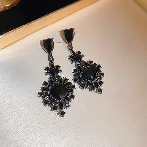 Detailed close-up of Gothic black heart earrings with sparkling crystals on white silk