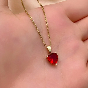 Close-up of heart-shaped red zircon necklace pendant on gold chain held in hand