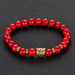 Detail of red stone beaded bracelet with golden owl charm and gear spacers on black texture