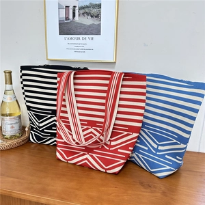 Three minimalist geometric striped knit tote bags in red, black and blue on a wooden table