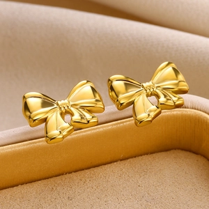 Macro shot of 18K gold-plated bow earrings on a jewelry box edge with mirror finish