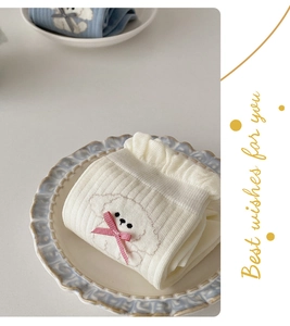 Close-up of white rib-knit socks featuring cute dog embroidery and a red ribbon bow detail