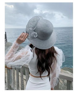 Detail of grey sun hat with organza flower decoration against a seaside background