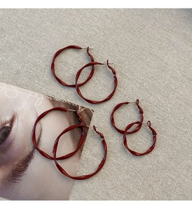 Three pairs of deep red irregular wavy metal hoop earrings in different sizes on linen
