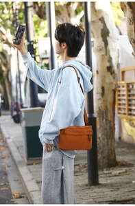 Detail of a burnt orange nylon crossbody bag with zipper pocket and wide strap
