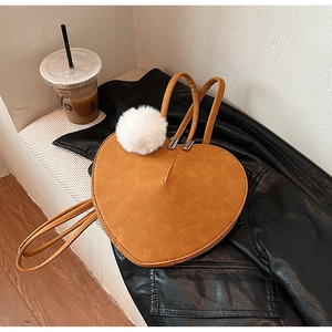 Detail der senfgelben herzförmigen Wildledertasche mit weißem Bommel-Accessoire