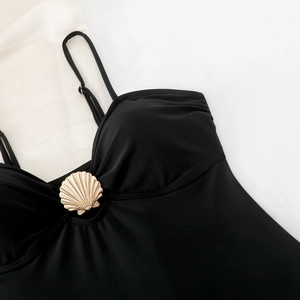 Detailed close-up of a black bikini top featuring a central golden metal shell ornament