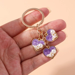 Detailed close-up of purple heart charms with white pearls on a gold-tone keychain accessory