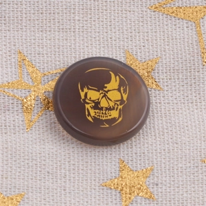 Close-up of a brown agate skull pendant with gold foil etching on linen background