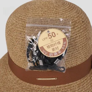 Detail of khaki straw sun hat with brown ribbon, UPF 50+ rating tag, and wind rope accessories