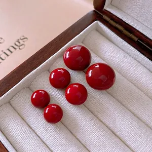 Polished red round stud earrings set in three different sizes on a velvet display tray