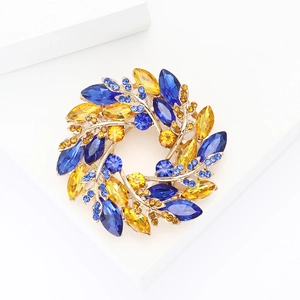 Elegant gold wreath brooch with blue and yellow rhinestones on a white display stand