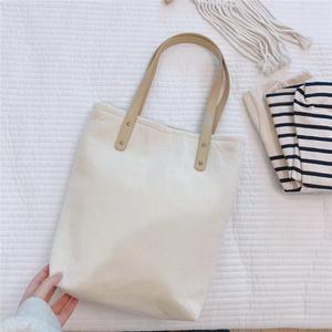 Detail of cream corduroy tote bag featuring brown leather handles and gold metal rivets