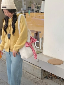 White faux shearling tote bag with large red plaid bow shown on a model's shoulder