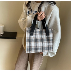 Detail of checkered canvas tote bag with black handles and metal snap button closure